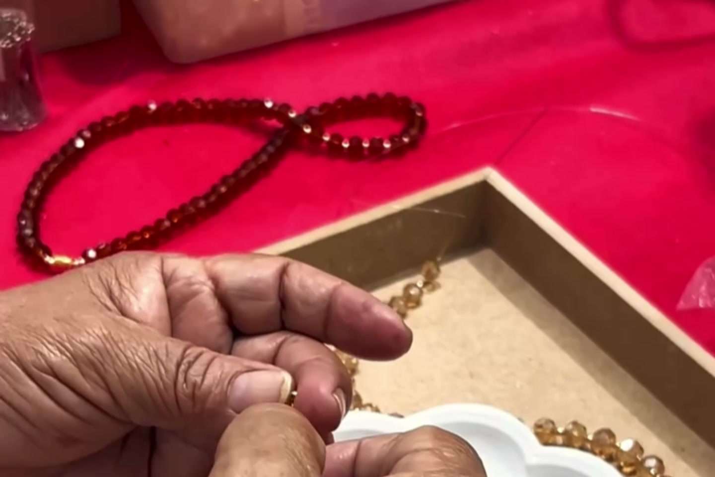 Mãos montando peça com contas âmbar na bandeja de acabamento